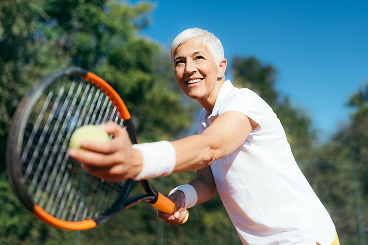 Older woman in position ready to serve tennis ball.