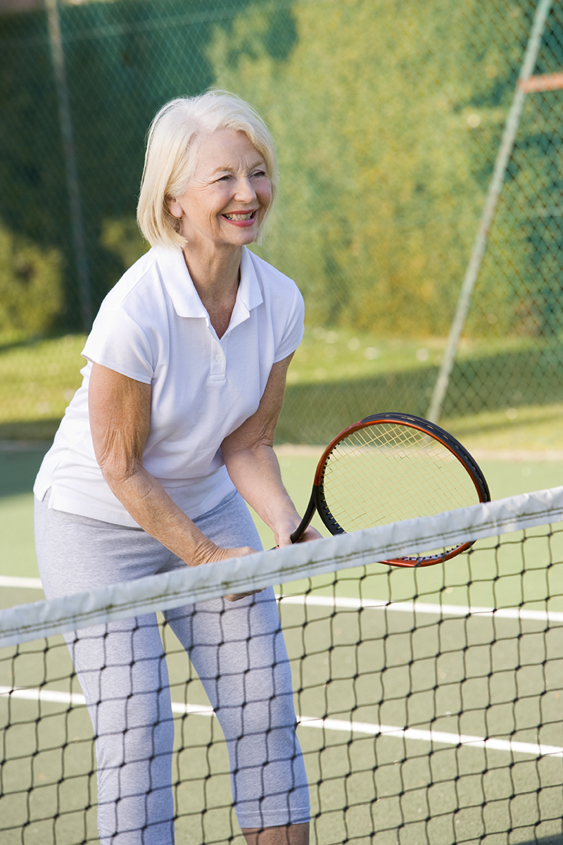 Older woman up close to tennis net ready to play